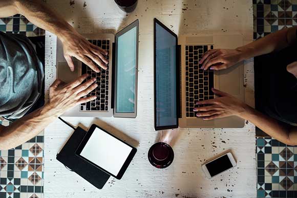 Two people with laptops back to back in workspace