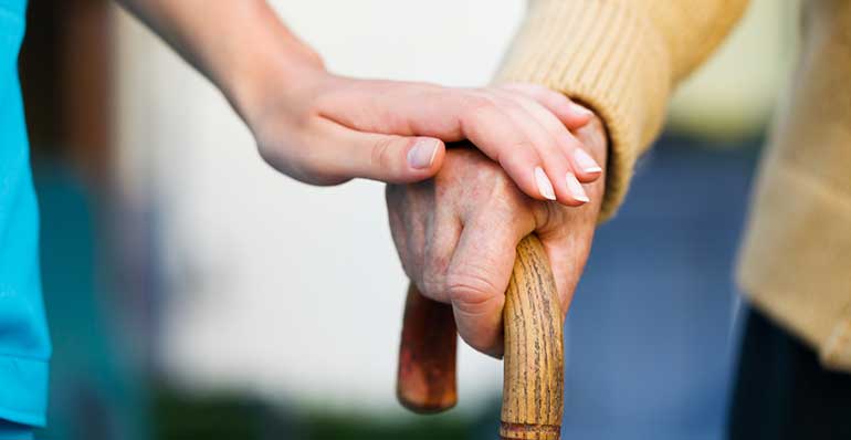 Aged care worker with patient hands on cane