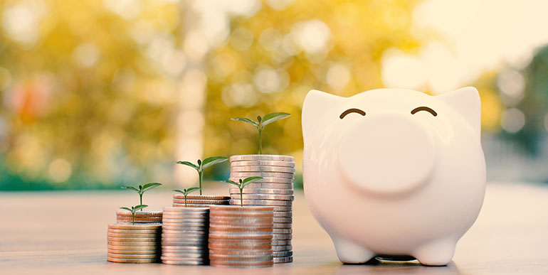 Happy piggy bank next to piles of coins