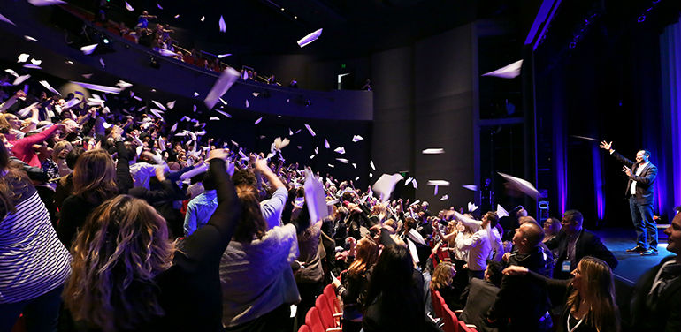 Man on stage throwing paper into the audience