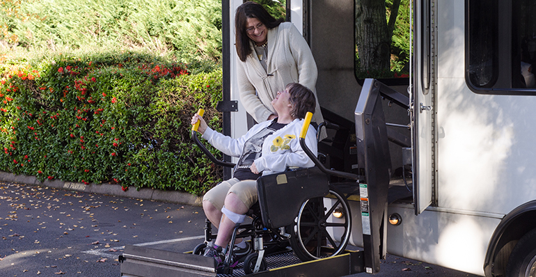 A woman in a wheelchair is helped off a van using a chair lift.