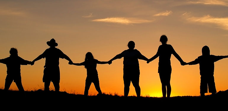 silhouette of chain of people standing against the sunset