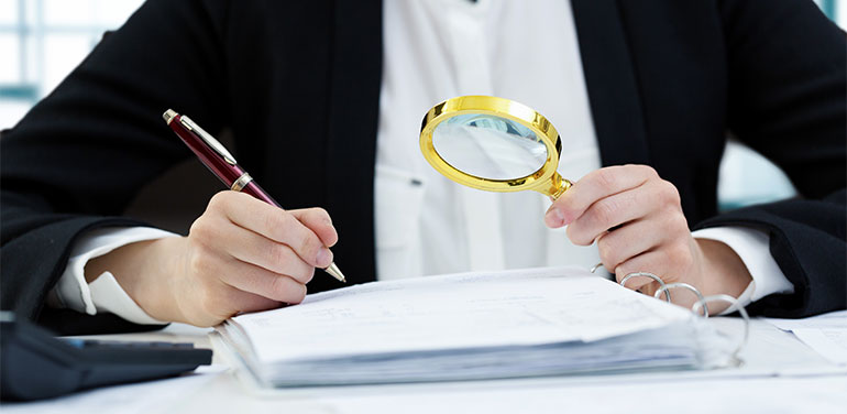 person looking through magnifying glass at documents