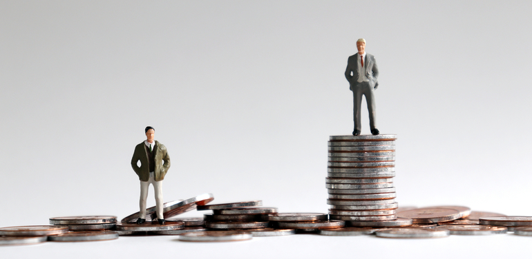 Miniature people standing on a pile of coins.