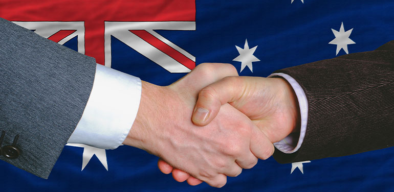 two hands shaking in front of Australian flag