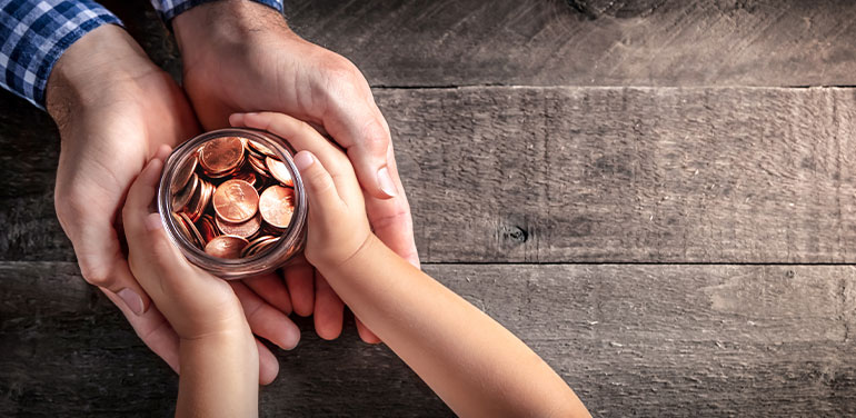 Mans hands holding childs hands with jar of coins