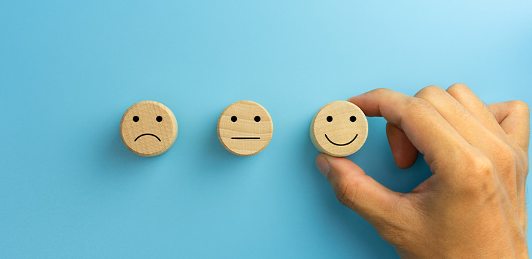 hand picking smile face icon on wooden cube on blue background.