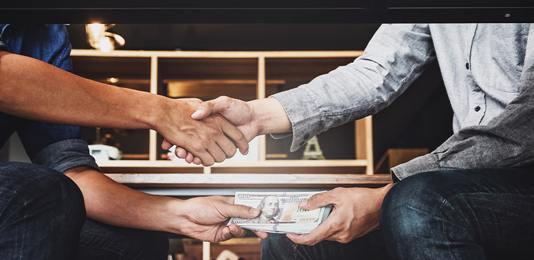 two men shaking hands and swapping money under the table