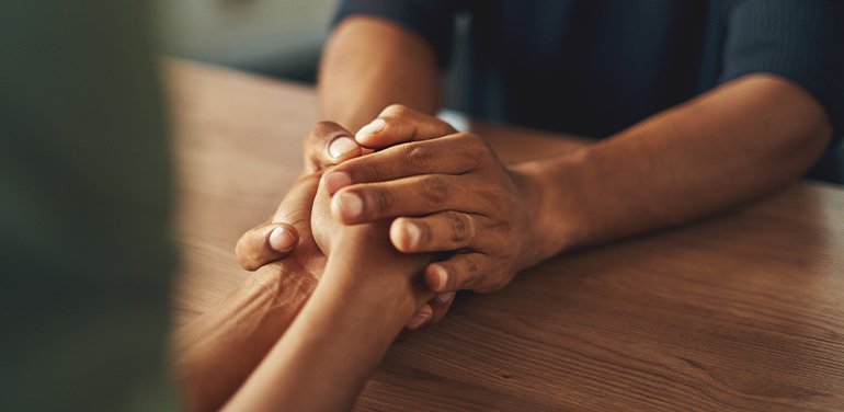 two pairs of hands on table, comforting