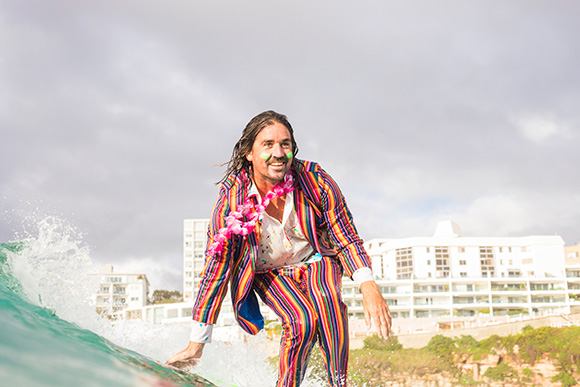 Grant on his surfboard wearing a fluro suit to raise awareness about mental health