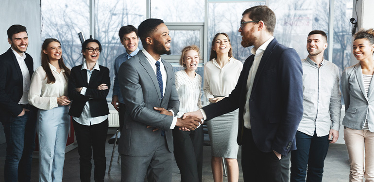 White man shaking hand with black employee in front of colleagues