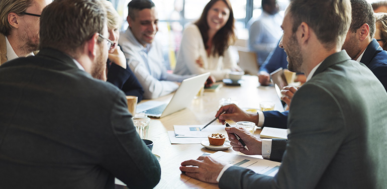 group of people sitting and smiling around a table having a board meeting