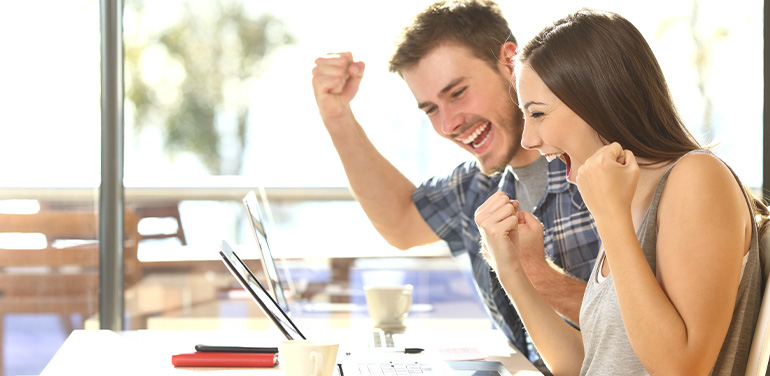 Happy couple celebrating looking at a laptop,