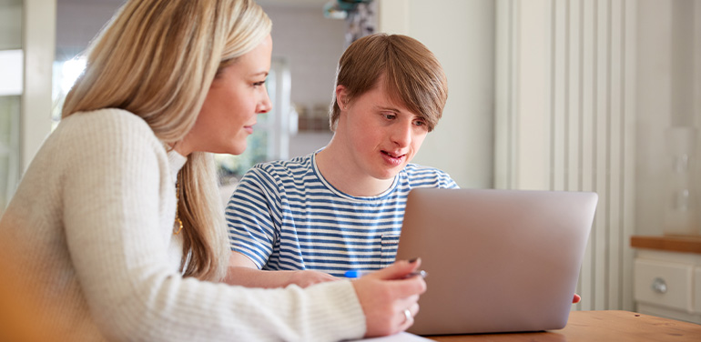 Man with down syndrome sat next to woman looking at a laptop