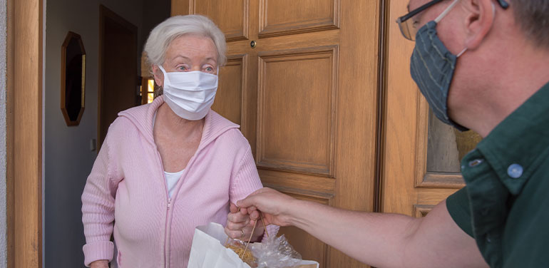 man handing a bag of food to an elderly lady at her front door.