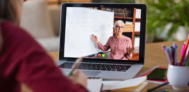 woman watching an online lesson on her laptop, on screen a woman is pointing at a whiteboard