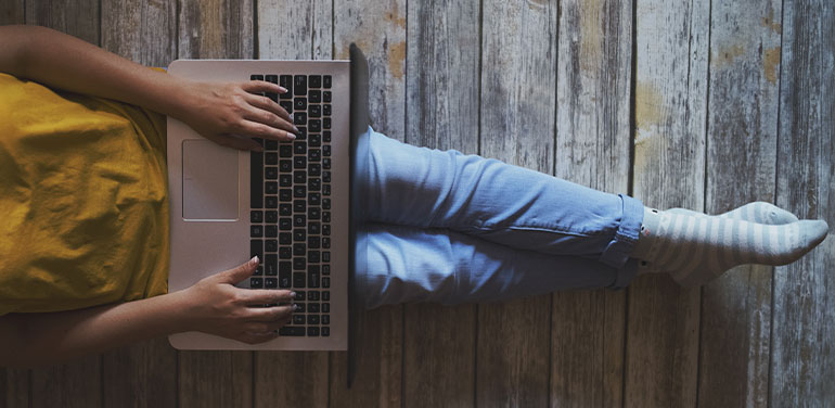 person working on laptop on their knee with legs stretched out in front of them