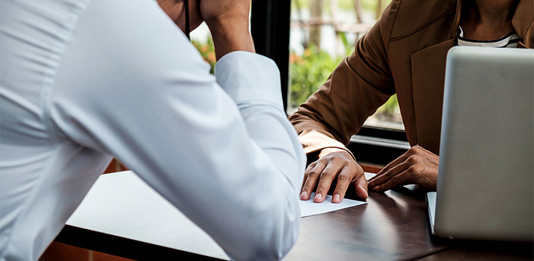 man sitting head in hands opposite manager giving him piece of paper