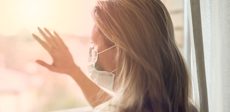 woman wearing a facemask, looking out of a window