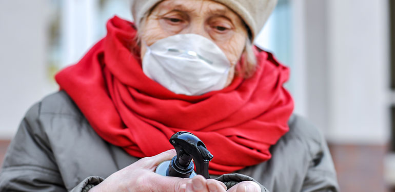 Close up of a woman wearing a face mask spraying her hands