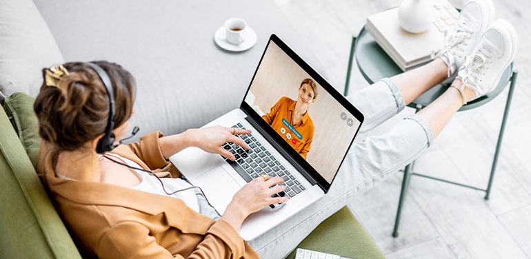 woman working from home, sitting on sofa with laptop on her knee