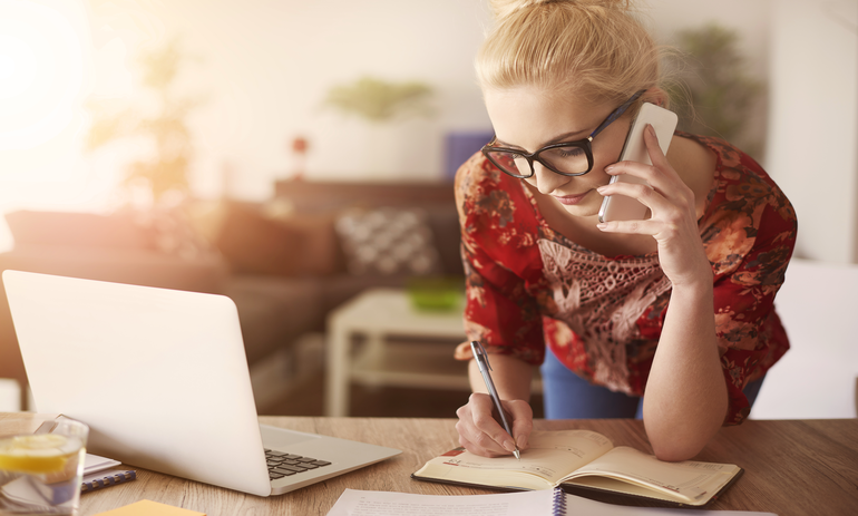 woman writing something in a notebook while she speaks on the phone