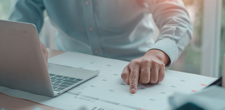 business man with laptop pointing at calendar on his desk