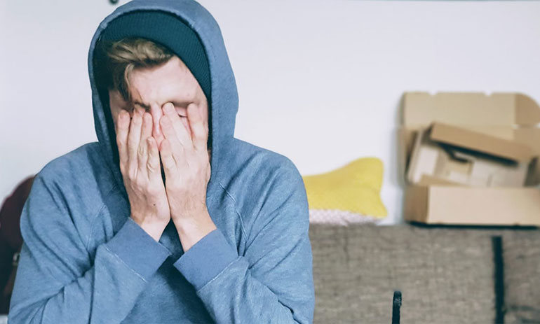 young man wearing blue hoodie with his head in his hands