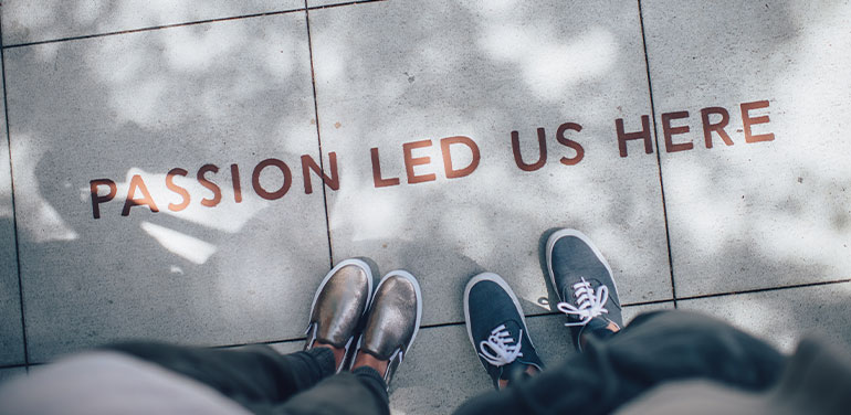 two pairs of feet next to writing on the pavement that says 'passion led us here'