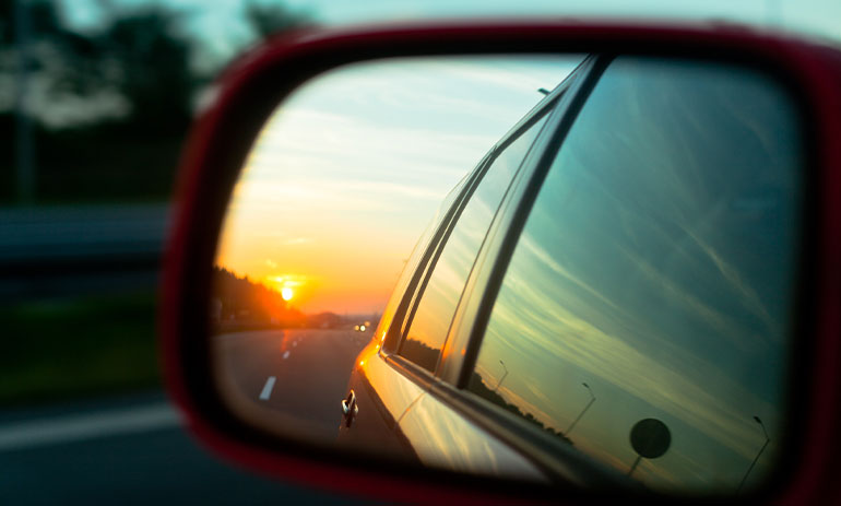 close up of a car rearview mirror showing the road behind