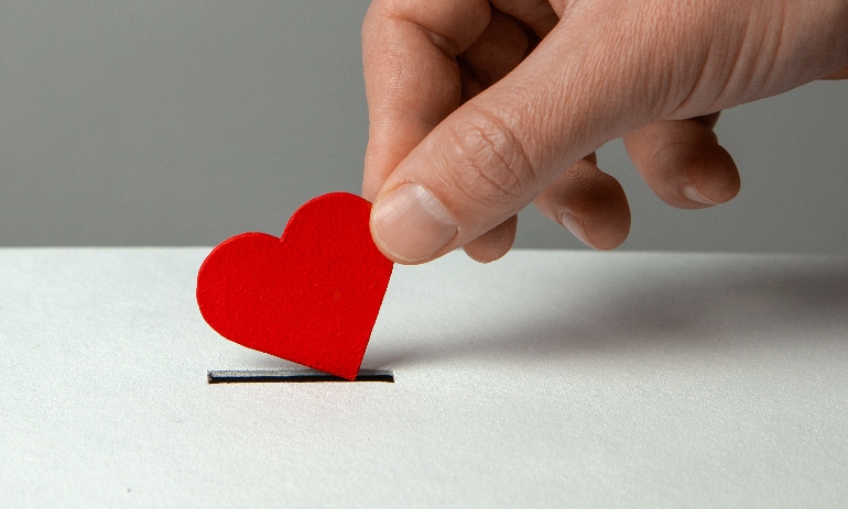 Man’s hand places heart in the donation slot.