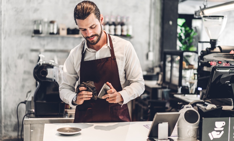 bearded barista man small business owner working behind the counter bar in a cafe