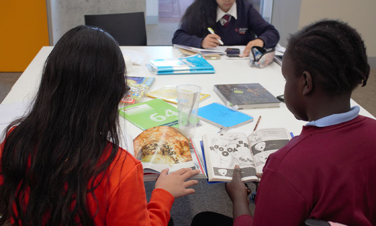 Two children in school sitting with their back to the camera working on something at a table