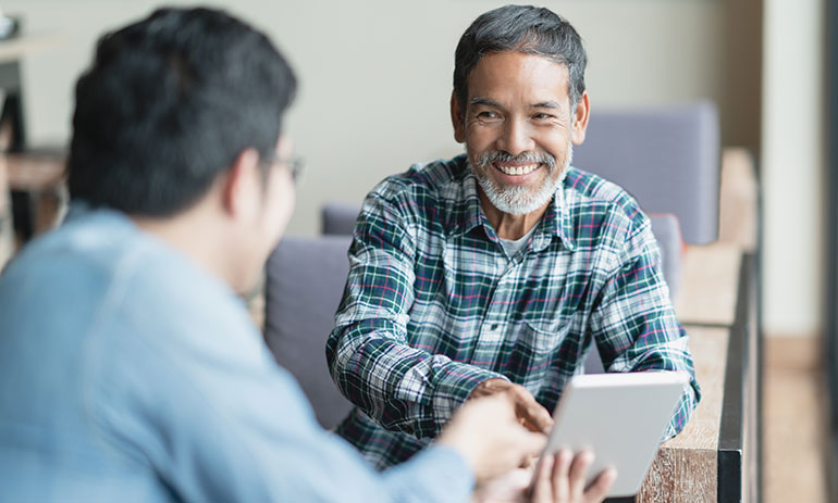 two men seated smiling shaking hands