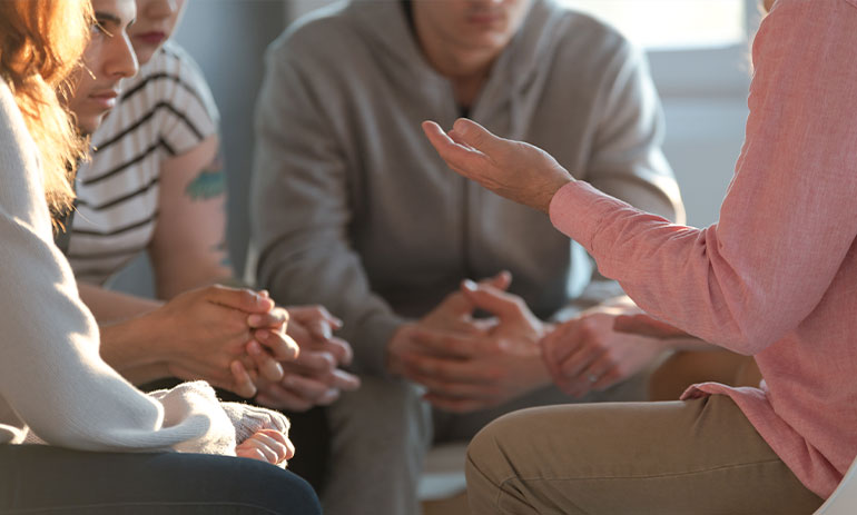 close up of group of people sitting in a circle talking at a support group