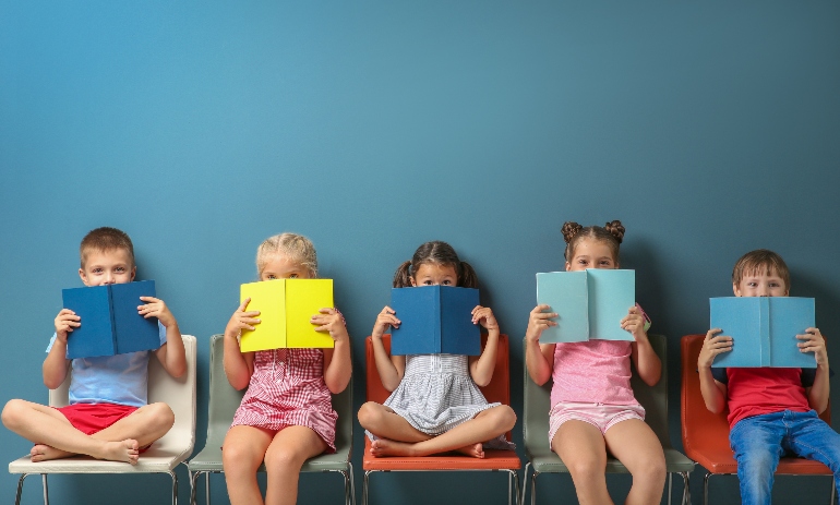 Cute little children reading books while sitting near color wall