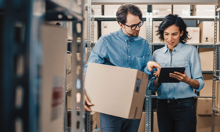 Female Inventory Manager Shows Digital Tablet Information to a Worker Holding Cardboard Box.