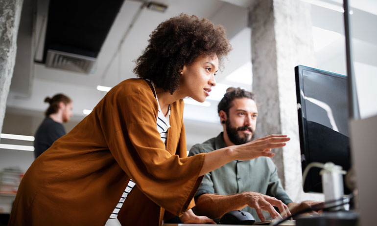 Woman of colour giving instructions to white man sat at a computer