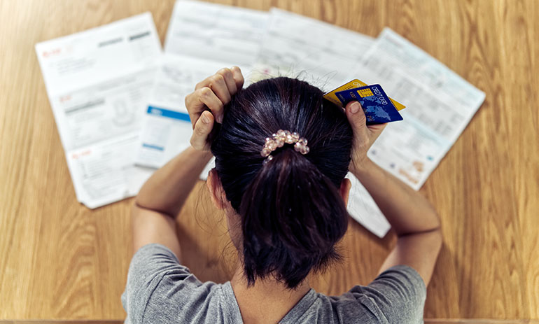 aerial view woman sat at a table with her hands on her head, looking at bills, holding a credit card