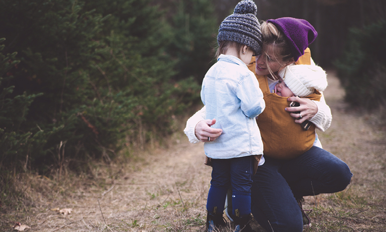 Mother holding a baby crouched down comforting a small child in a forest