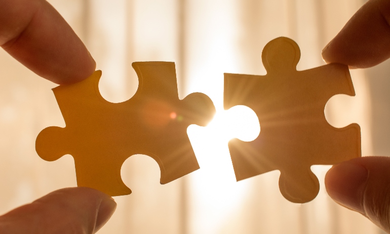 two hands trying to connect couple puzzle piece. with sunset background. symbol of association and connection, business strategy, completing, team support and help concept