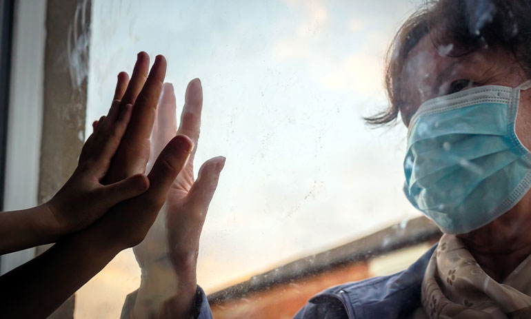 a woman wearing a facemask touching her hand to a window, with hand touching the other side