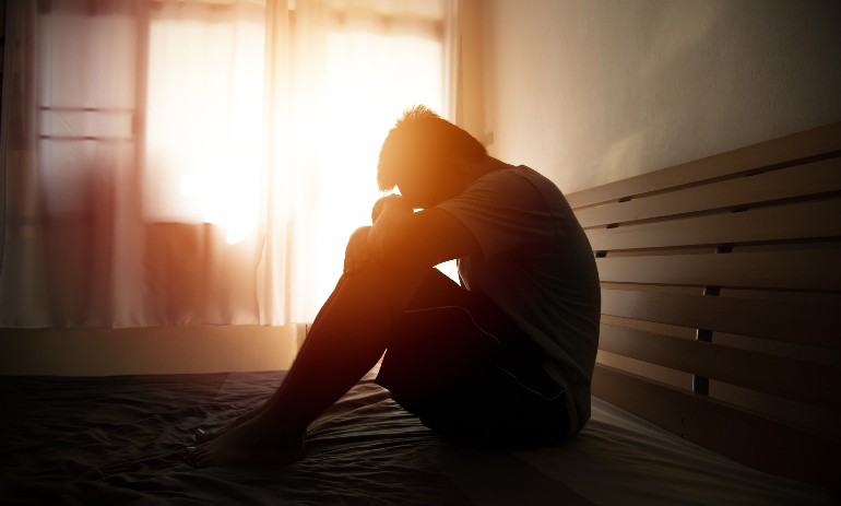 desperate man in silhouette sitting on the bed with hands on head