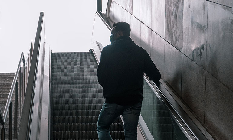 Man wearing facemask walking up an escalator