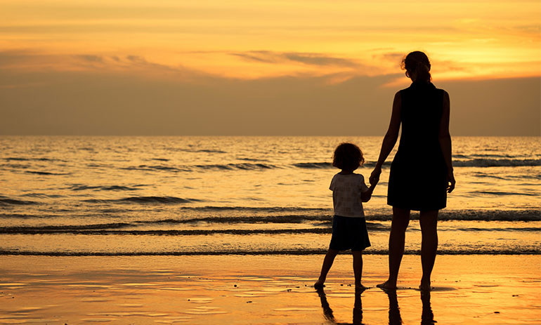 Mother and son at the beach at sunset looking out to the sea