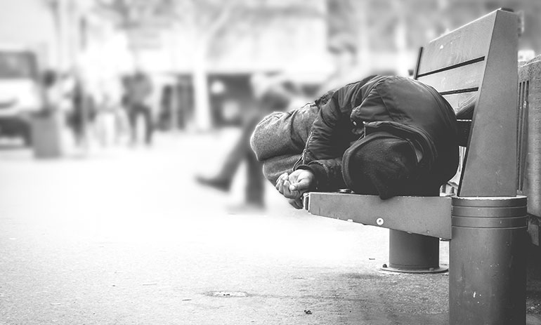 black and white image of man sleeping on a park bench