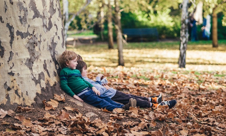 Three children sat leaning against a tree, surrounded by leaves