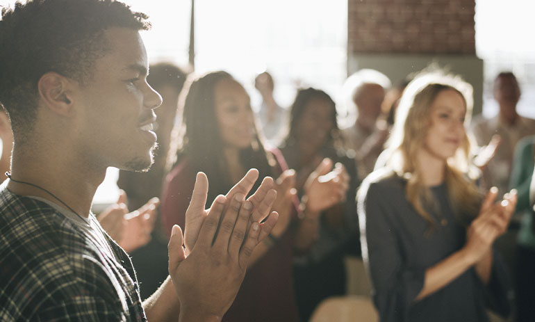 A diverse group of people clapping at a community meeting.