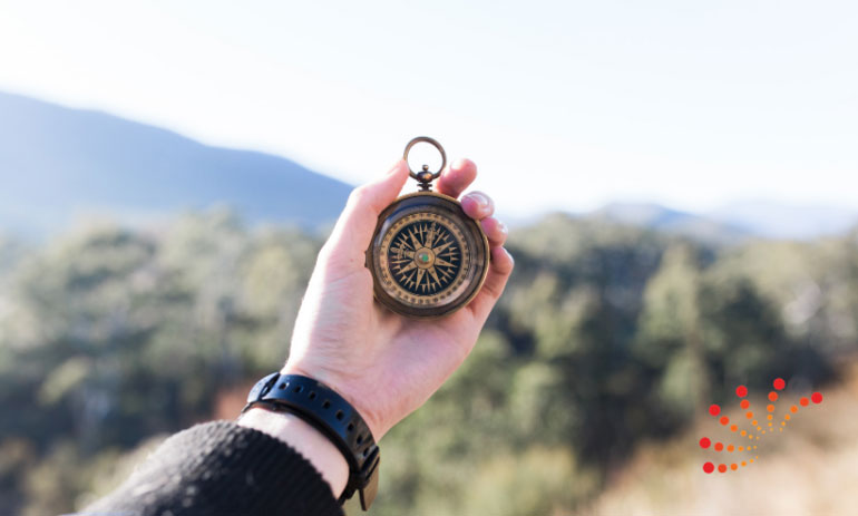 hand holding a compass out with a mountain and trees in the background