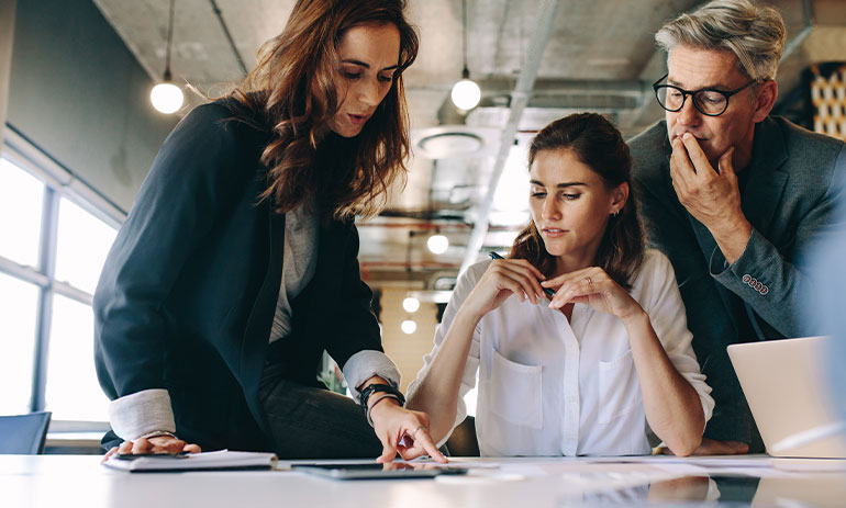 three people standing around a desk looking at paper